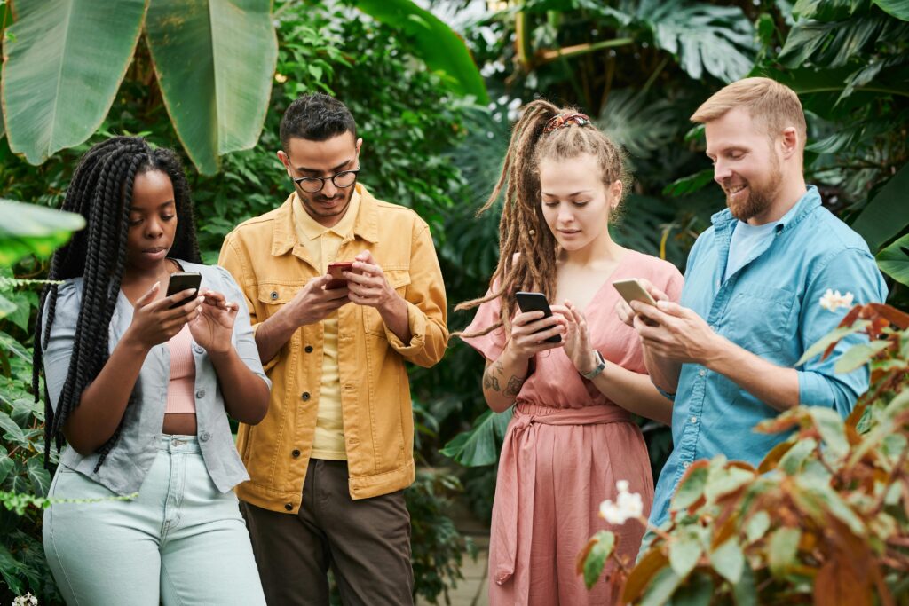 Four adults using smartphones surrounded by lush greenery in an outdoor setting, enjoying technology in nature.